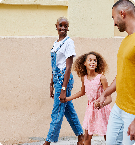 A group of people walk together, smiling and holding hands, against a pastel-colored wall.