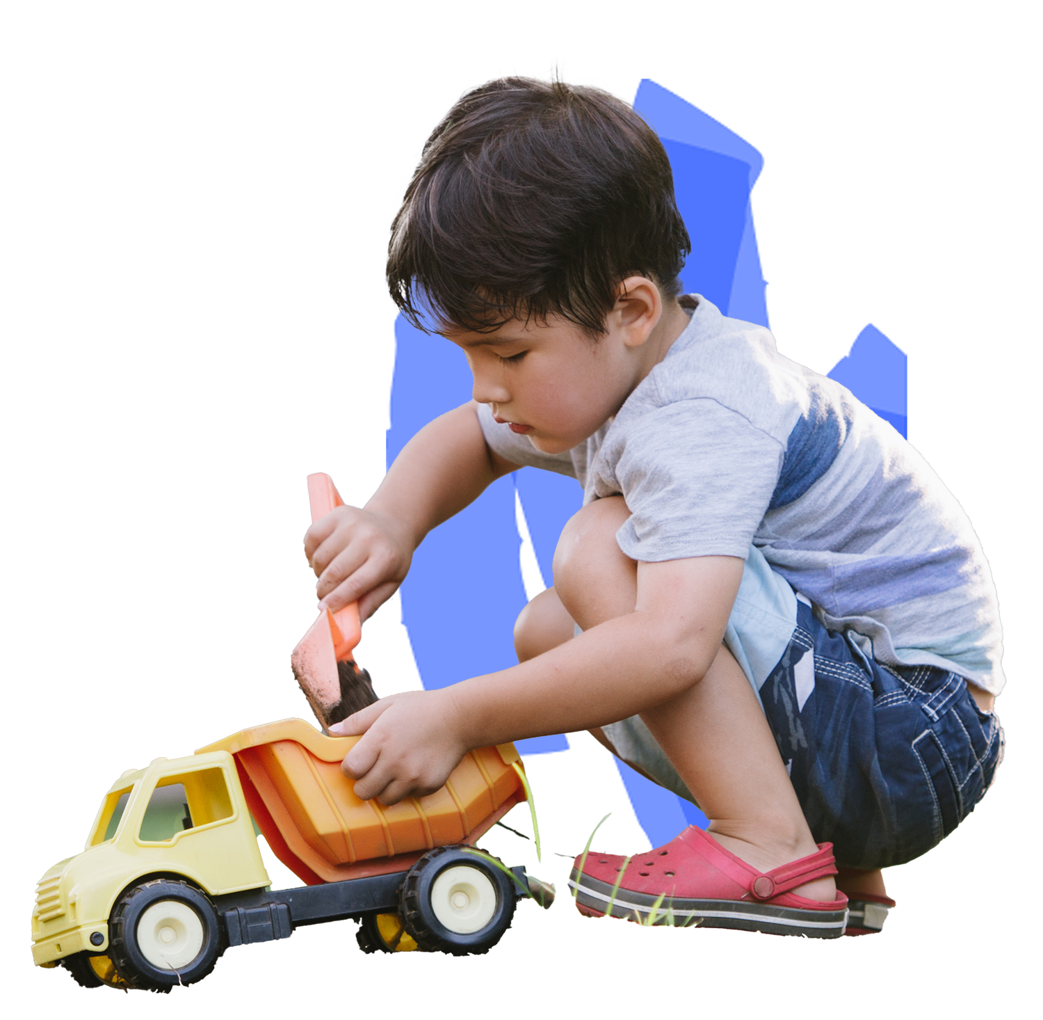 A child in casual clothing plays with a toy truck while using a small shovel.